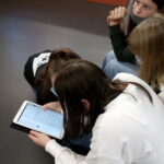 Na zdjęciu widać trzy dziewczynki czytające wyświetlony na tablecie tekst.